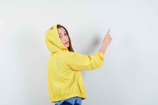 Young lady pointing up in t-shirt, jacket and looking hesitant .