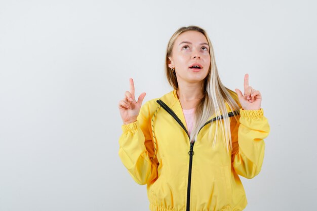 Young lady pointing up in t-shirt, jacket and looking puzzled