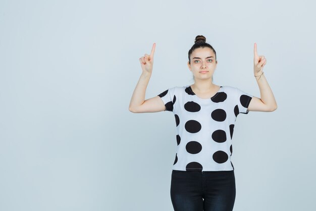 Young lady pointing up in t-shirt, jeans and looking confident , front view.