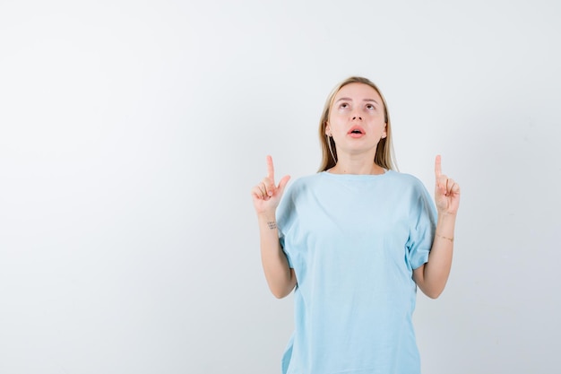 Free photo young lady pointing up in t-shirt and looking puzzled isolated