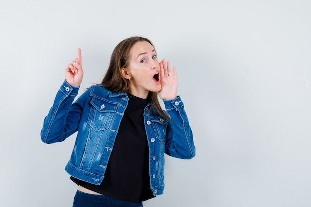 Free photo young lady pointing up while telling secret in blouse, jacket and looking curious , front view.