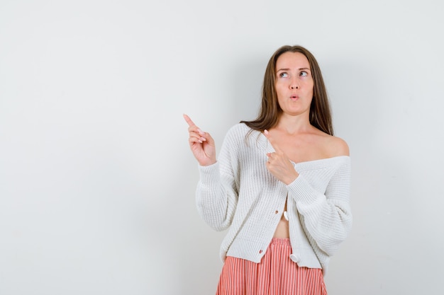 Young lady pointing at upper left corner in cardigan and skirt looking hesitant isolated