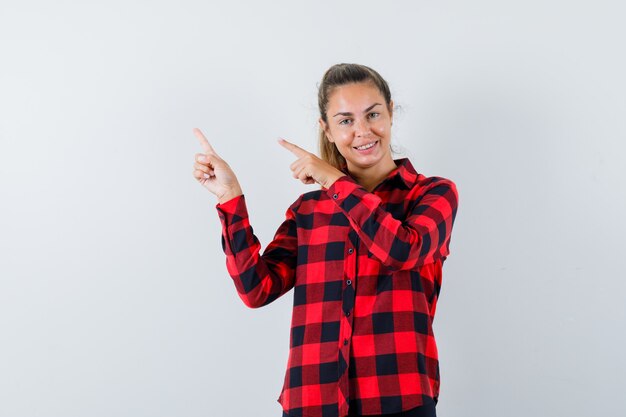 Young lady pointing at upper left corner in checked shirt and looking cheerful