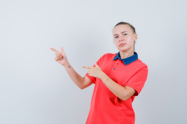 Young lady pointing at upper left corner in t-shirt and looking confident