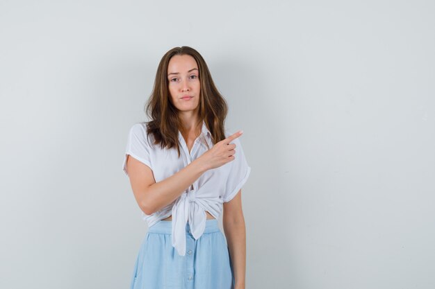 Young lady pointing at upper right corner in blouse and skirt and looking confident