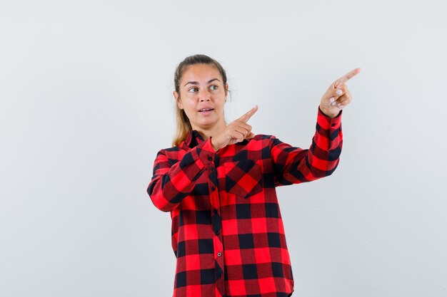 Young lady pointing at upper right corner in checked shirt and looking focused