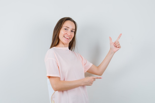 Young lady pointing at upper right corner in pink t-shirt and looking merry , front view.