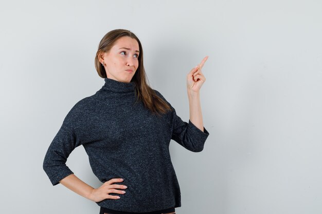 Young lady pointing at upper right corner in shirt and looking hesitant