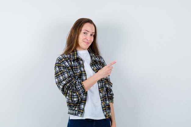 Young lady pointing at upper right corner in t-shirt, jacket and looking confident. front view.