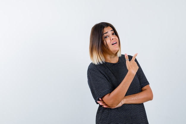 Young lady in polo dress pointing aside and looking puzzled , front view.