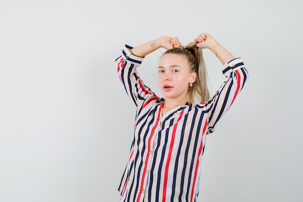 Young lady posing while pulling hair in striped shirt and looking stylish