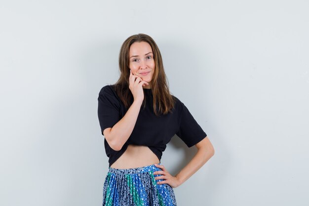 Young lady posing while standing in blouse, skirt and looking alluring