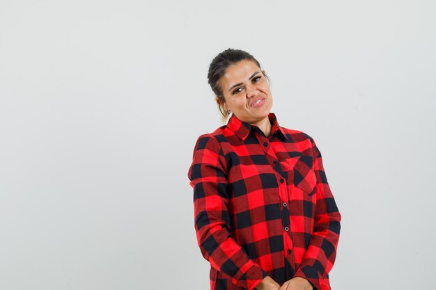 Young lady posing while standing in checked shirt and looking jovial. 