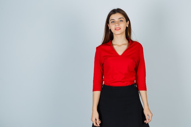 Молодая дама позирует, стоя в красной блузке, юбке и нежно выглядит