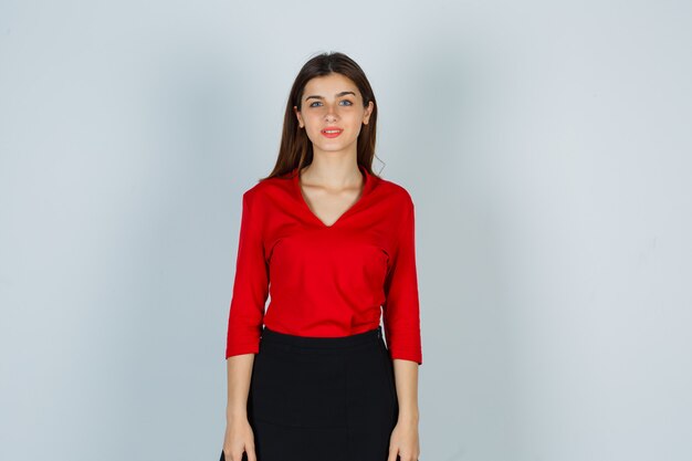 Young lady posing while standing in red blouse, skirt and looking gorgeous