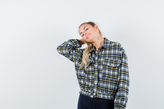 Giovane signora che posa con la mano dietro la testa in camicia, pantaloncini e sembra delizioso. vista frontale.