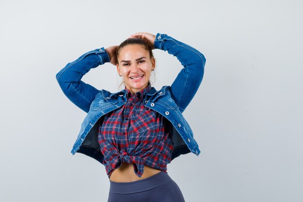 Young lady posing with hands behind head in shirt, jacket and looking merry , front view.