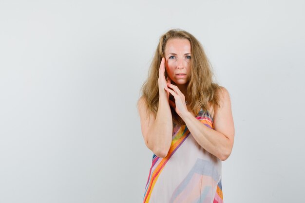 Young lady posing with palm near cheek in summer dress and looking nice 