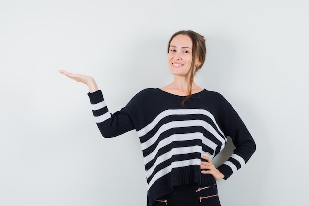 Young lady presenting something in casual shirt and looking merry