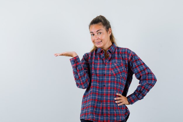 Young lady presenting something in checked shirt and looking merry. front view.