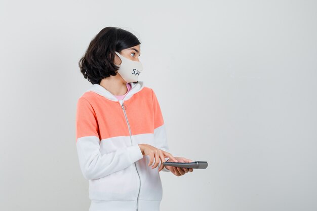 Young lady pressing calculators button in hoodie, face mask and looking puzzled