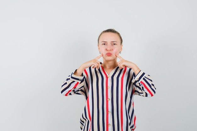 Young lady pressing fingers on blown cheeks in striped shirt