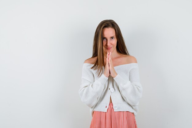 Young lady pressing hands together to pray in cardigan isolated