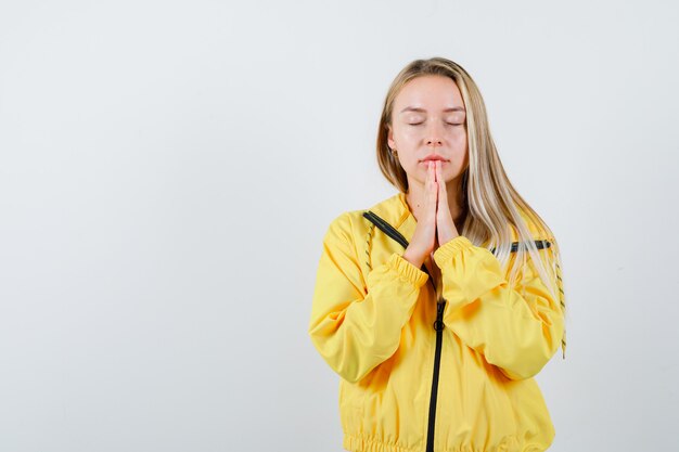 Young lady pressing hands together while praying in t-shirt, jacket and looking peaceful