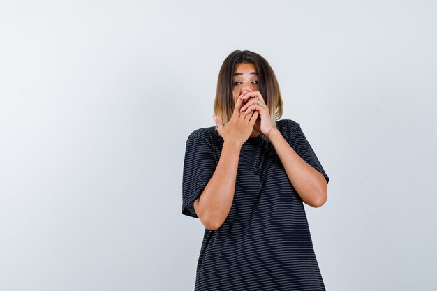 Young lady pressing nose with hands in polo dress and looking funny , front view.