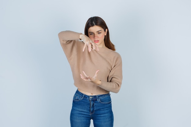 Young lady pretending to catch something in beige sweater, jeans and looking focused , front view.