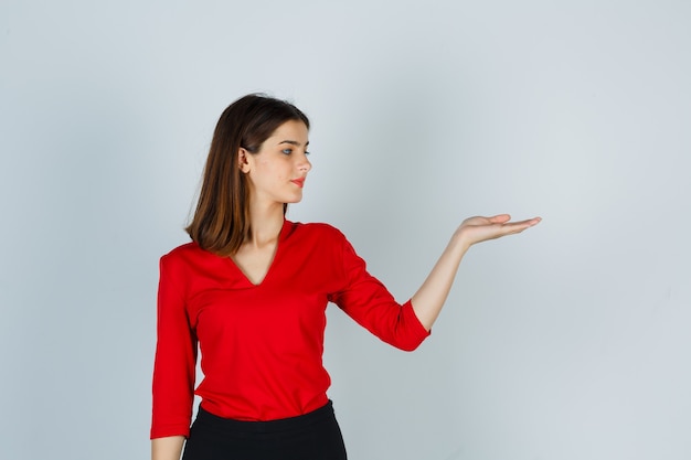 Young lady pretending to hold something in red blouse, skirt and looking confident