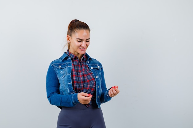 Young lady pretending to hold something while looking down in shirt, jacket and looking jolly , front view.