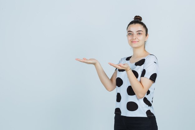 Tシャツ、ジーンズ、自信を持って、正面から何かを見せているふりをしている若い女性。