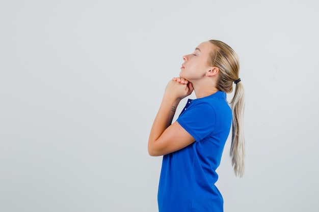 Young lady propping chin on clasped hands in blue t-shirt and looking hopeful .