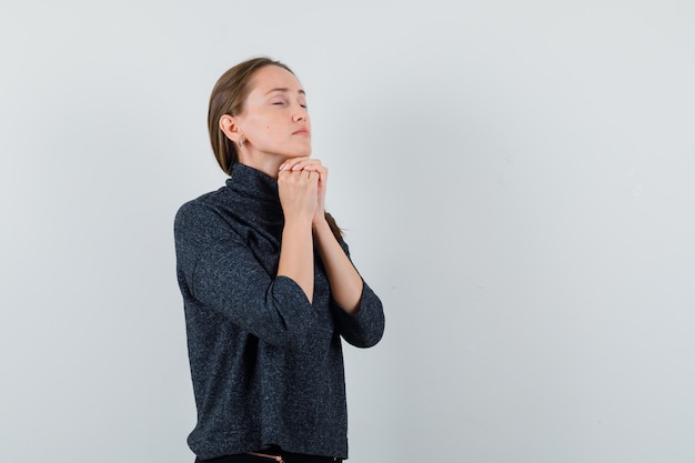 Giovane donna appoggiando il mento sulle mani giunte in camicia casual e guardando speranzoso