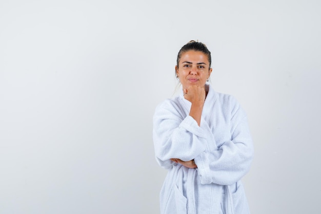 Young lady propping chin on fist in bathrobe and looking confident