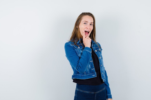 Young lady propping chin on hand in blouse, jacket and looking happy , front view.