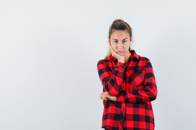 Young lady propping chin on hand in checked shirt and looking pensive