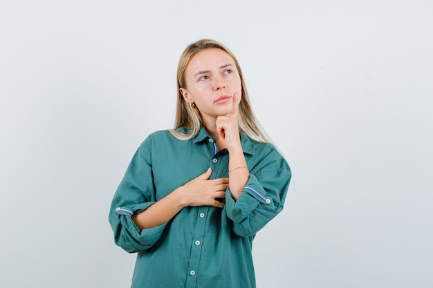 Young lady propping chin on hand in green shirt and looking pensive