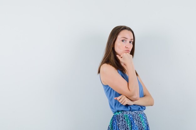 Young lady propping chin on hand in singlet, skirt and looking sensible