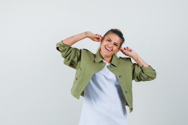 Young lady pulling her ears in t-shirt jacket and looking amused  