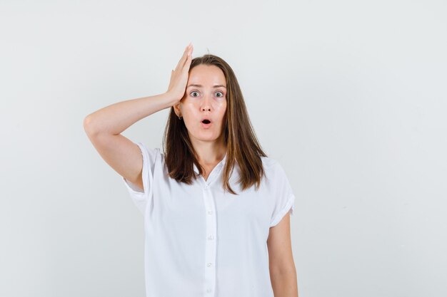 Young lady putting her hand on head in white blouse and looking troubled.