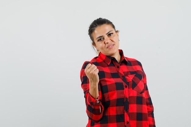 Young lady raising clenched fist in checked shirt and looking confident