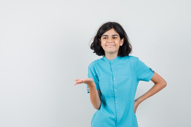 Young lady raising hand with open palm for expressing something in blue shirt and looking pleased.