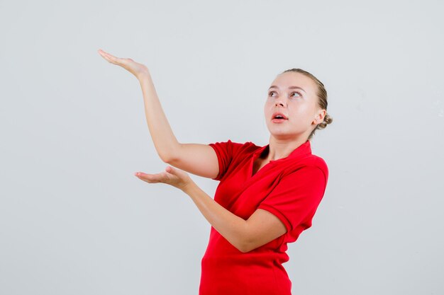 Young lady raising hands as holding something in red t-shirt