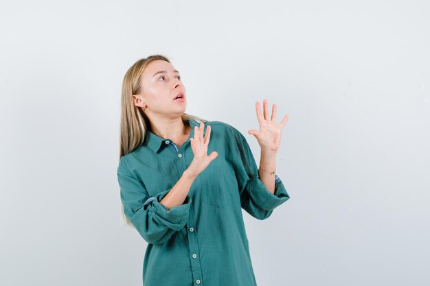 Young lady raising hands to defend herself in green shirt and looking scared.