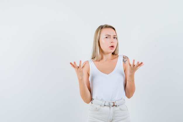 Young lady raising hands with open palm up in white blouse and looking puzzled