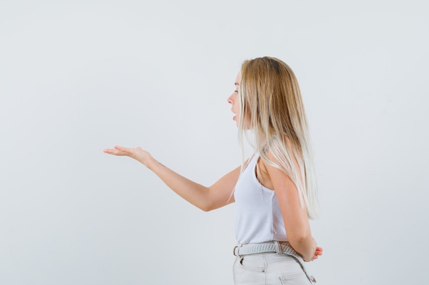 Foto gratuita giovane donna alzando la mano con modo aggressivo in camicetta bianca e guardando concentrato.