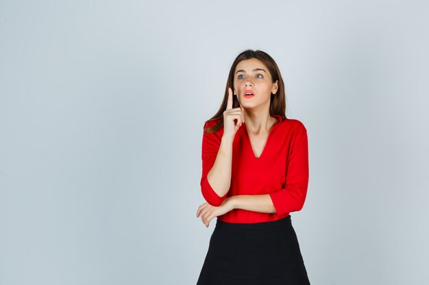 Young lady raising index finger in eureka gesture in red blouse