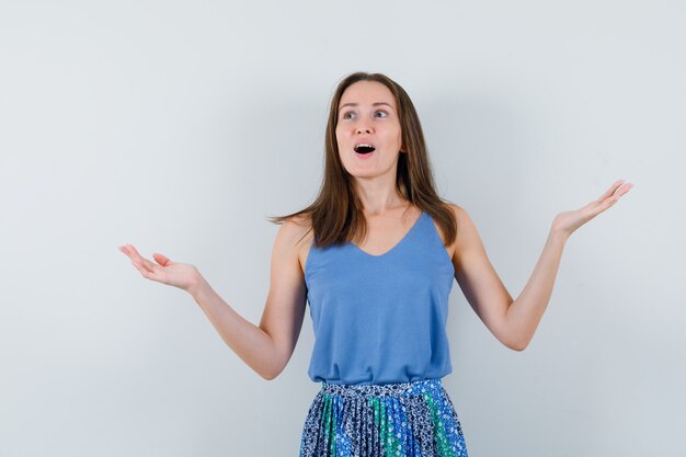 Young lady raising open palms in singlet, skirt and looking dreamy